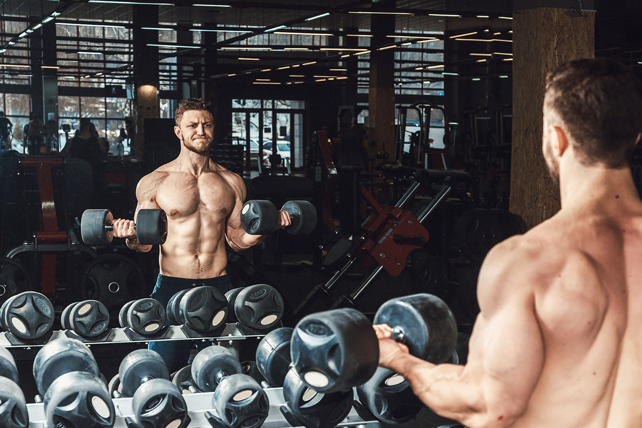 Muscular Guy Doing Bicep Curls In Front of a Mirror